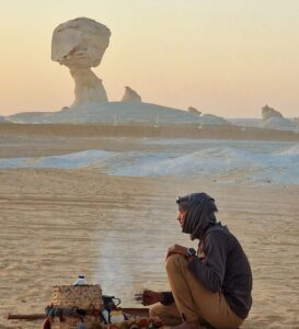A local Bedouin guide preparing traditional tea over a campfire in the White Desert, showcasing the authentic cultural immersion of our Egypt desert safari packages.