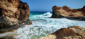 Vibrant turquoise water crashing against rugged rocks, showcasing the incredible natural contrasts found on a Fayoum desert getaway.
