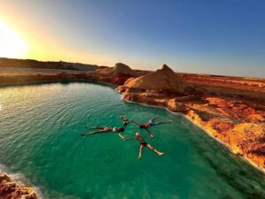 Four people floating in a star formation within a bright turquoise emerald desert lake, a unique and safe experience offered on a Fayoum desert getaway.